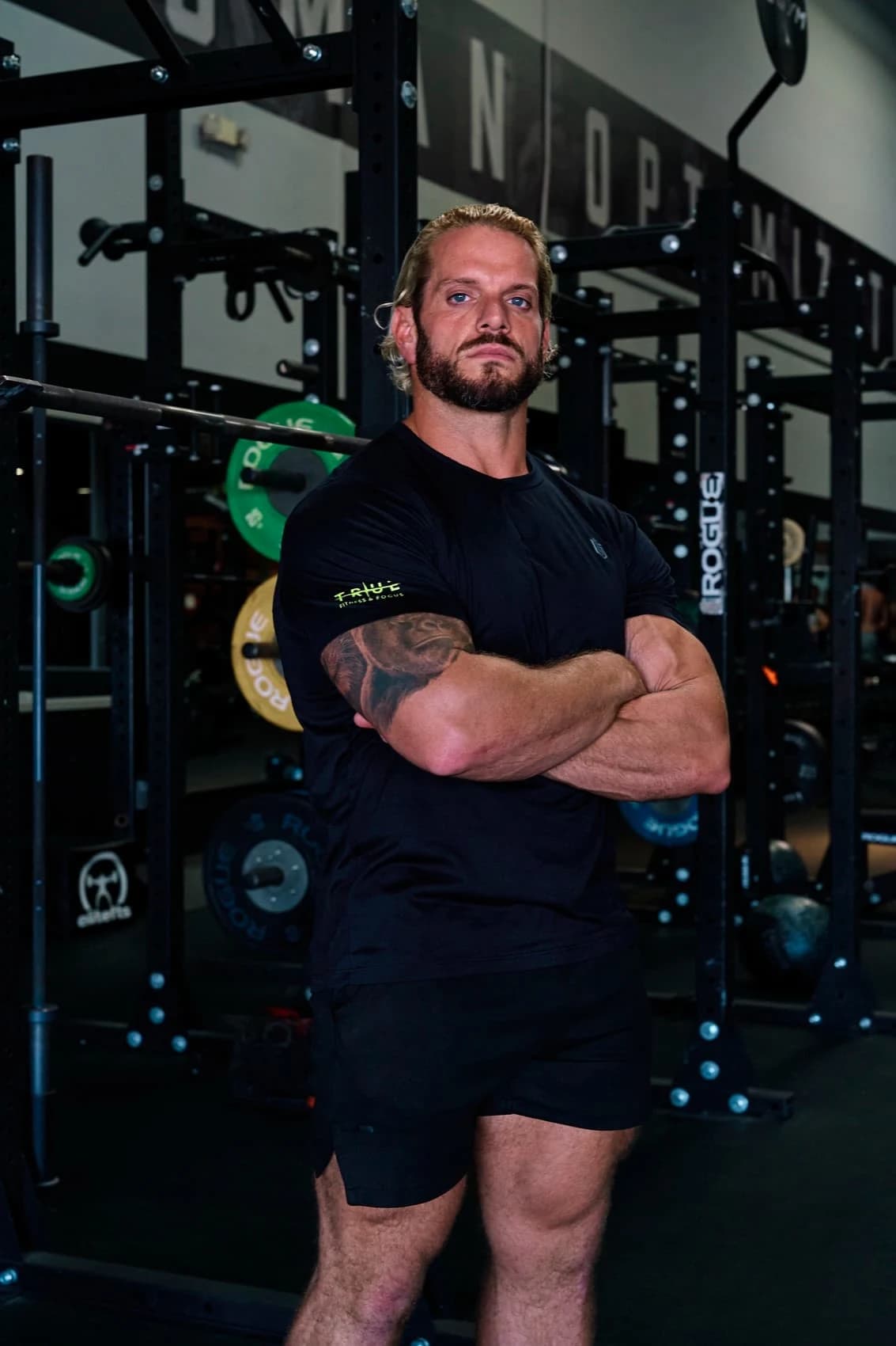 Jarred Curcio standing with his arms crossed by the squat racks in the gym in Austin, Texas