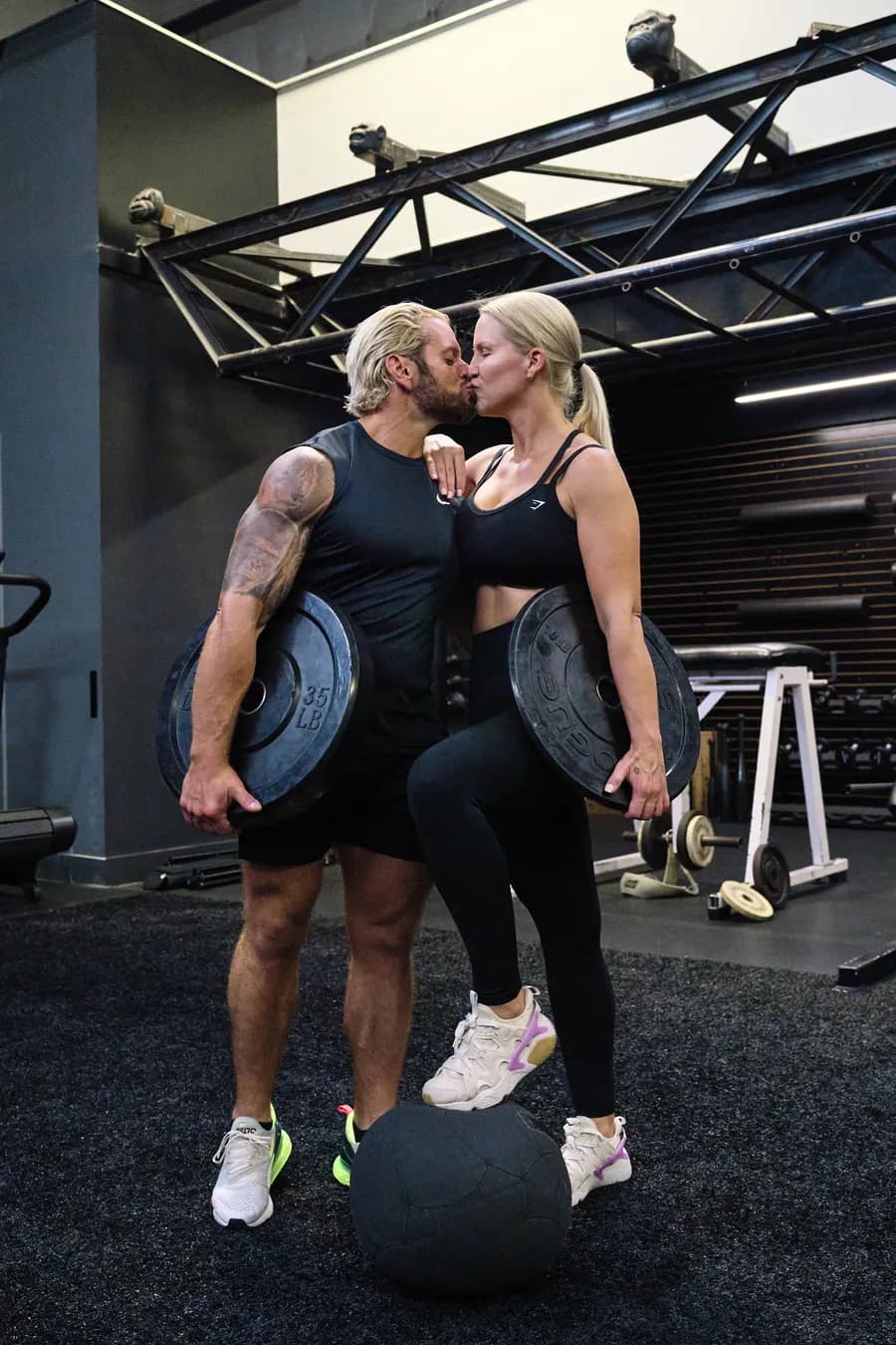 Jarred and Katelyn Curcio kissing and holding weight plates in the gym in Austin, Texas
