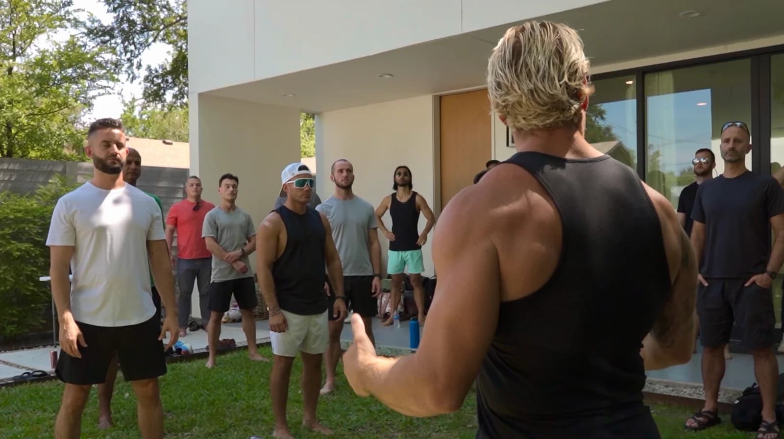 Jarred Curcio with his back to the camera addressing a group of men in a front yard in Austin, Texas