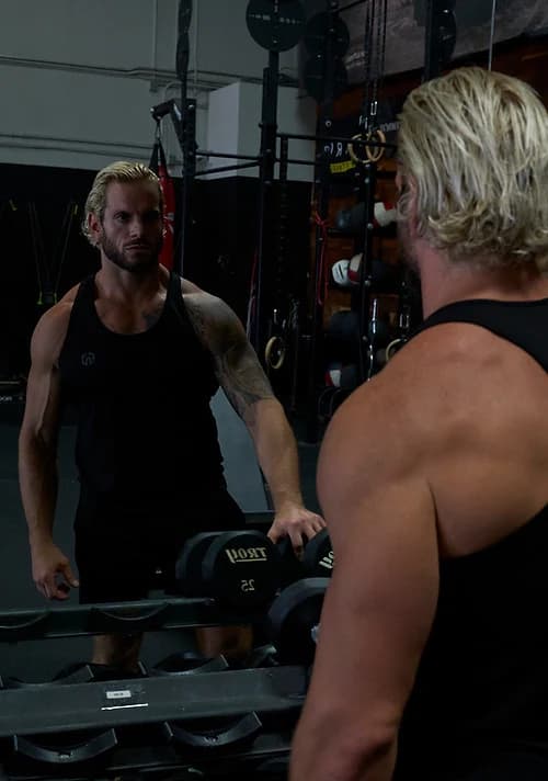 Jarred Curcio facing his reflection with dumbbells in the gym in Austin, Texas